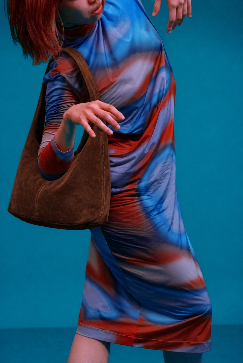 Brown suede hobo bag carried against a teal backdrop
